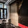 En roddmaskin och träningscykel står stilla i ett svagt upplyst gym med industristil, med synliga rör och en rå betongvägg med sektioner i rött och svart.