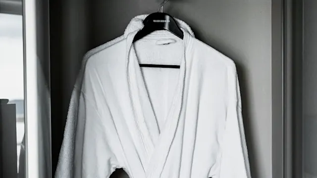 Hvit badekåpe hengende på en svart henger i et garderobeskap med glassdører. Tekst på hengeren sier: "YOU LOOK GOOD IN ME". 