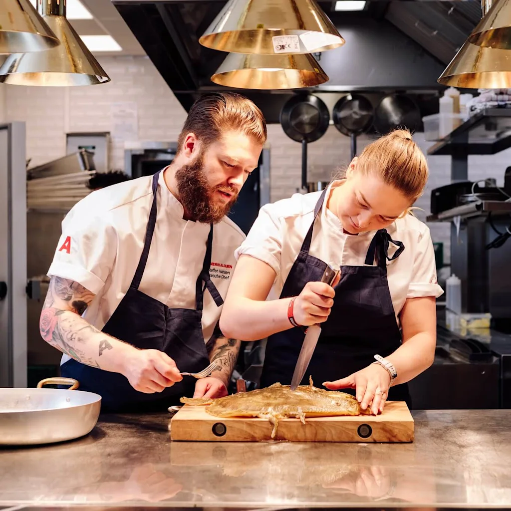 Two chefs cooking fish in a restaurant kitchen.