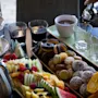 Tallerkener med oppskåret frukt, bakverk og fargerike makroner ordnet på et bord med to glass og en kaffekopp. En hånd heller fra en metallkanne. Svakt opplyst spisemiljø.