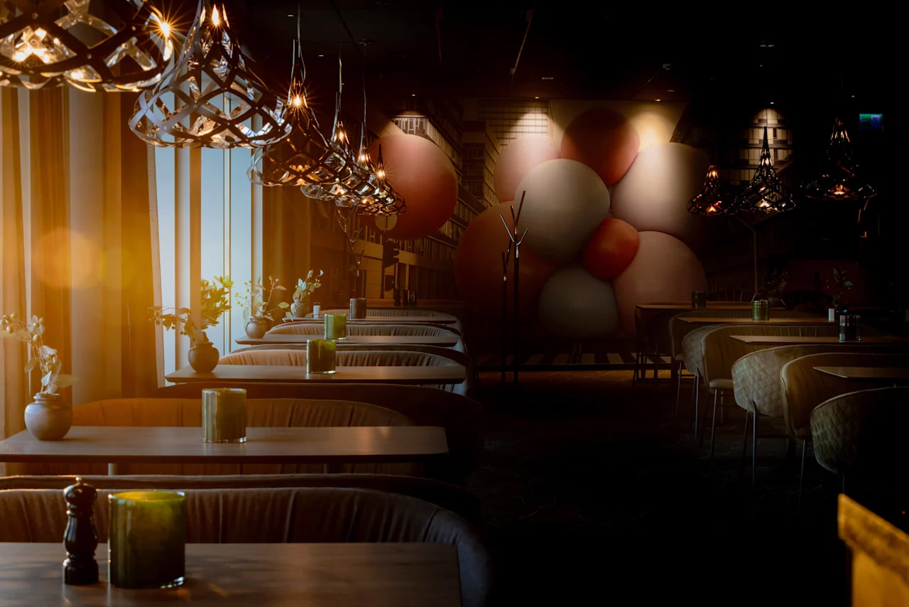 Norwegian Bokmål: Bord med grønne lys er stilt opp under moderne pendellamper, i en svakt opplyst restaurant med et veggmaleri av store overlappende sfærer.