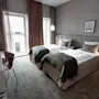 Två sängar med vita lakan och gröna filtar står i ett prydligt rum, med ett skrivbord och stol till vänster och ett fönster med gardiner i bakgrunden.