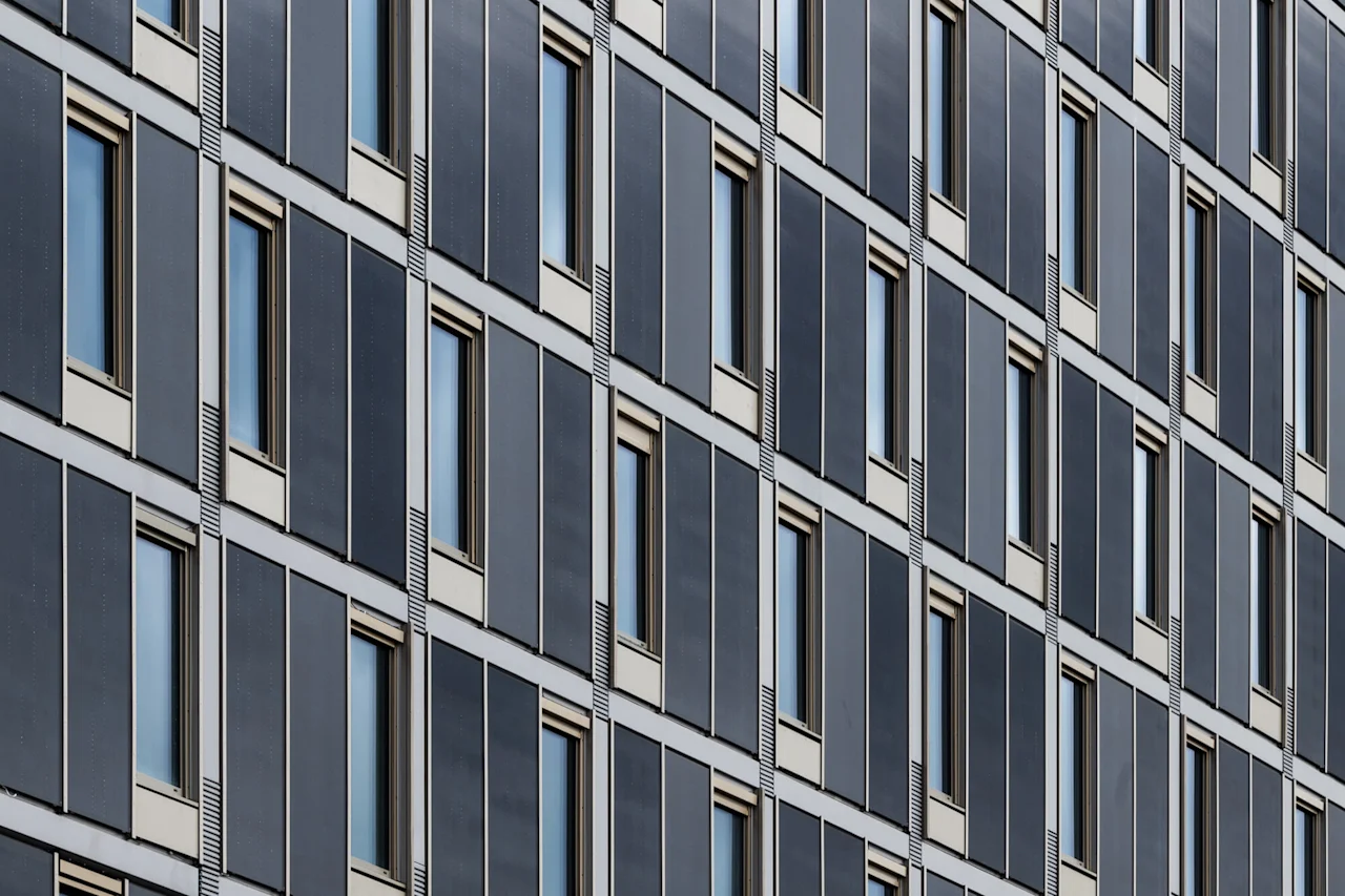 Ett repetitivt arkitektoniskt mönster av en modern byggnadsfasad med många fönster och metallklädsel, fångat diagonalt.