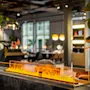 En rektangulær, moderne peis avgir lysende oransje flammer i et stilfullt, plantefylt innemiljø, som skaper en varm, innbydende atmosfære blant moderne møblement.