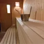 En trebadstue har en bøtte og øse på en benk, med varmt lys og en lukket dør i bakgrunnen.