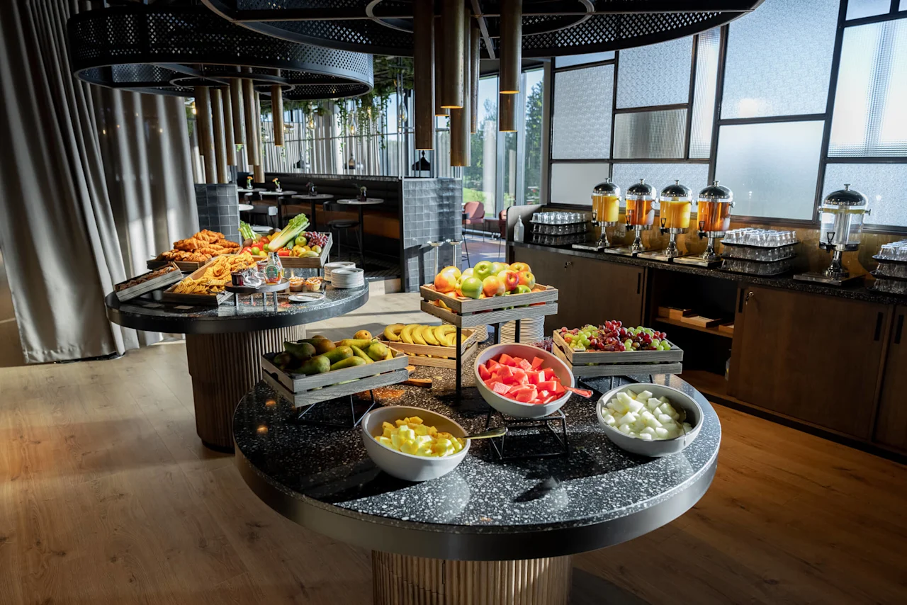 En frokostbuffé med assortert frukt og drikkevarer i et moderne spiseområde.