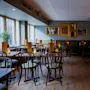 Empty restaurant interior with arranged tables and chairs, warm lighting from pendant lamps, framed pictures on the walls.