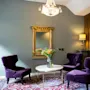 Elegant room with purple armchairs, a marble table, and a large ornate mirror, bathed in soft lighting, on a patterned rug.