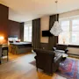 A well-appointed room with a large bed, desk, chairs, a chandelier, and a round mirror on a colored wall, suggesting a luxurious interior setting.
