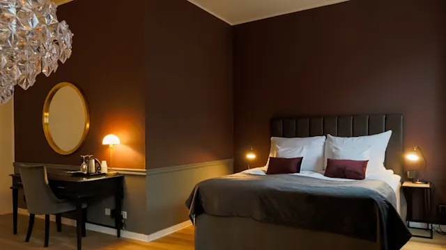 Elegant bedroom with dim lighting illuminates a large bed, side tables, and a desk, showcasing a cozy ambiance.