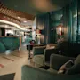 Comfortable armchairs are arranged for relaxation in a dimly lit lounge area with curtains, subdued lighting, and a counter in the background.