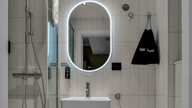 Nykyajan kylpyhuone, jossa taustavalaistu peili, suihku, pesuallas ja wc minimalistisessa tyylissä. Seinällä teksti "Hair Dryer".