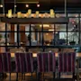 Et langt spisebord med stripete stoler i en elegant restaurant. Over er en hylle med tente lys, og myk belysning skaper en koselig atmosfære.