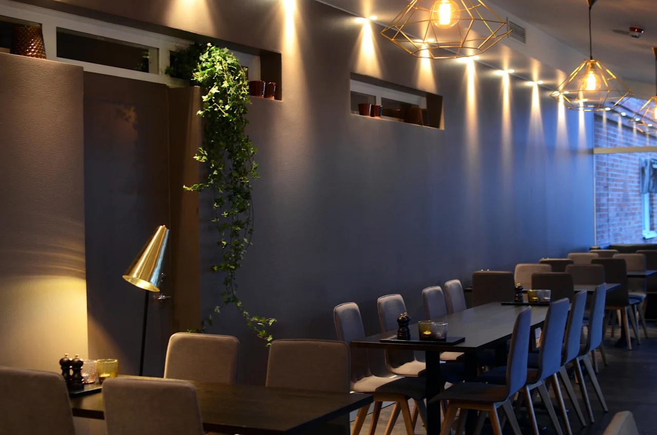 Modernt restauranginteriör med geometriska hängande lampor, klädda stolar och mörka bord, framhävt med varm och sval belysning, ger en mysig atmosfär.