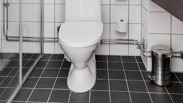 Ett modernt badrum med vit toalett, handdukshängare och duschhörna av glas. Svartvitt kaklat golv med rena linjer.