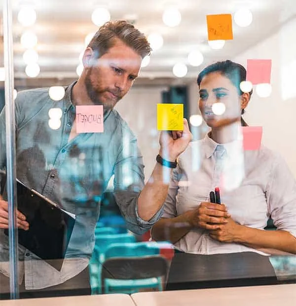 Colleagues writing on post-its stuck to glass wall