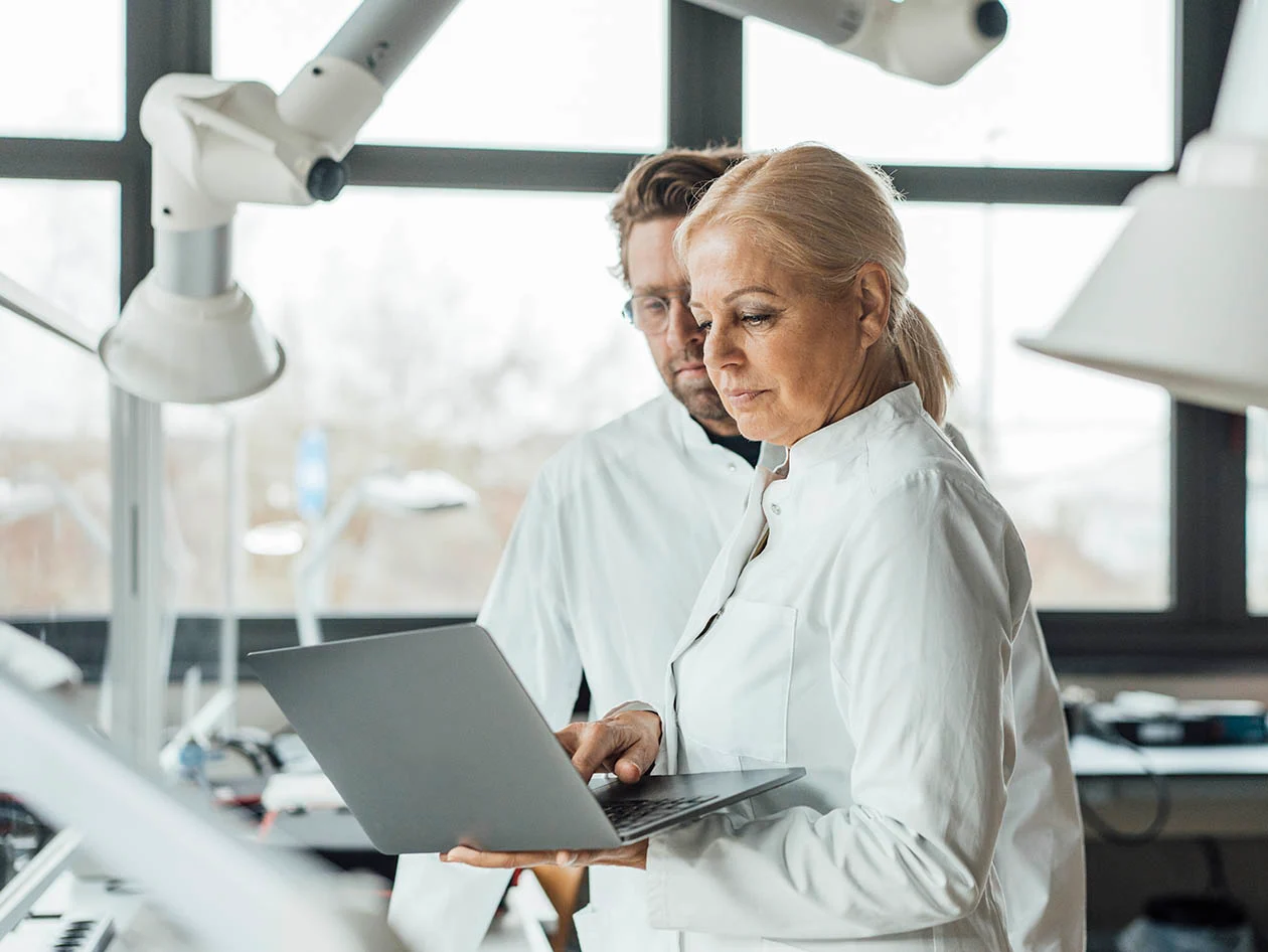 Photo conveying two R&D researchers in white coats collaborating at a laptop. (Westend61 via Getty Images)