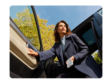 Femme sortant de sa voiture avec son téléphone à la main.
