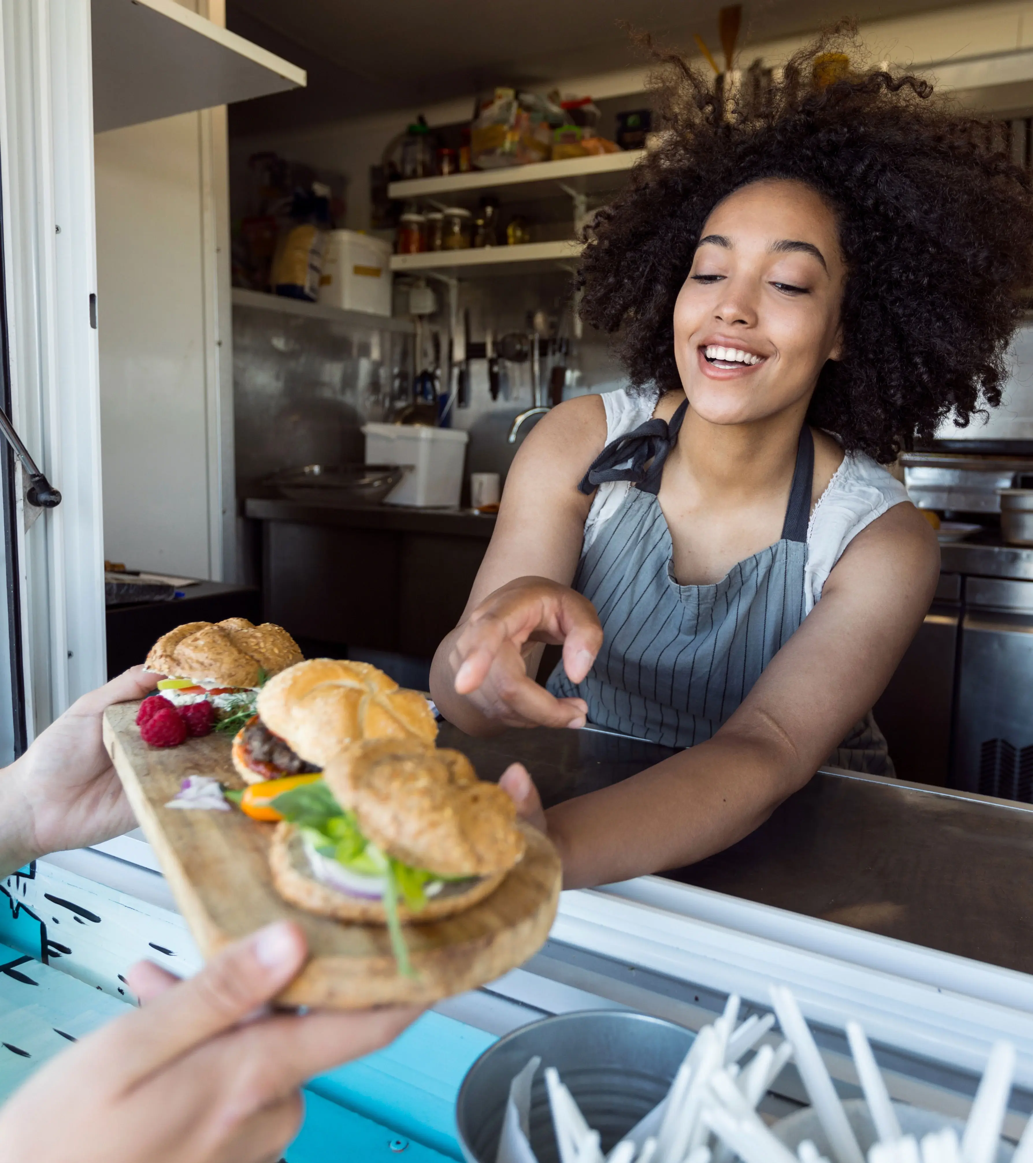 Image of a kitchen employee holding a wooden board with three appetizers, passing it over a counter to a customer.