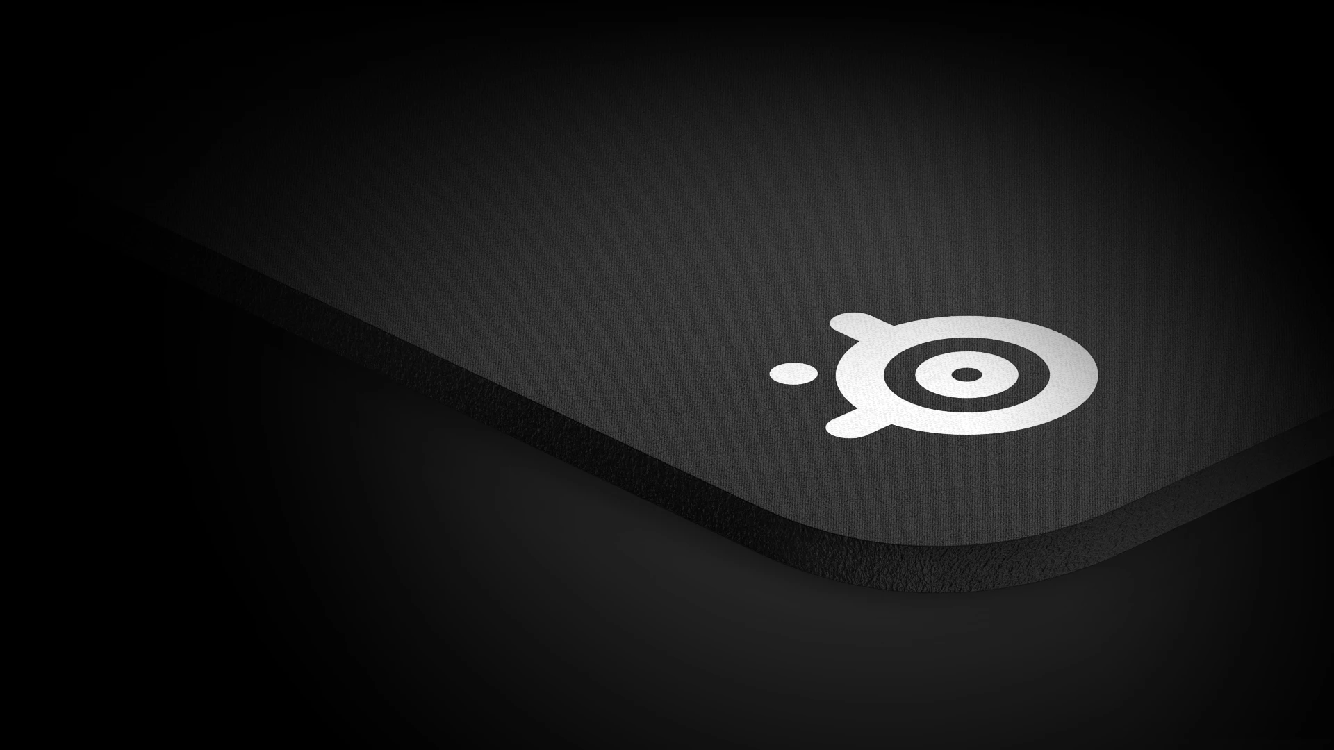 Üzerinde büyük beyaz steelseries logosu bulunan qck ağır mousepad'in bir köşesine bakış.