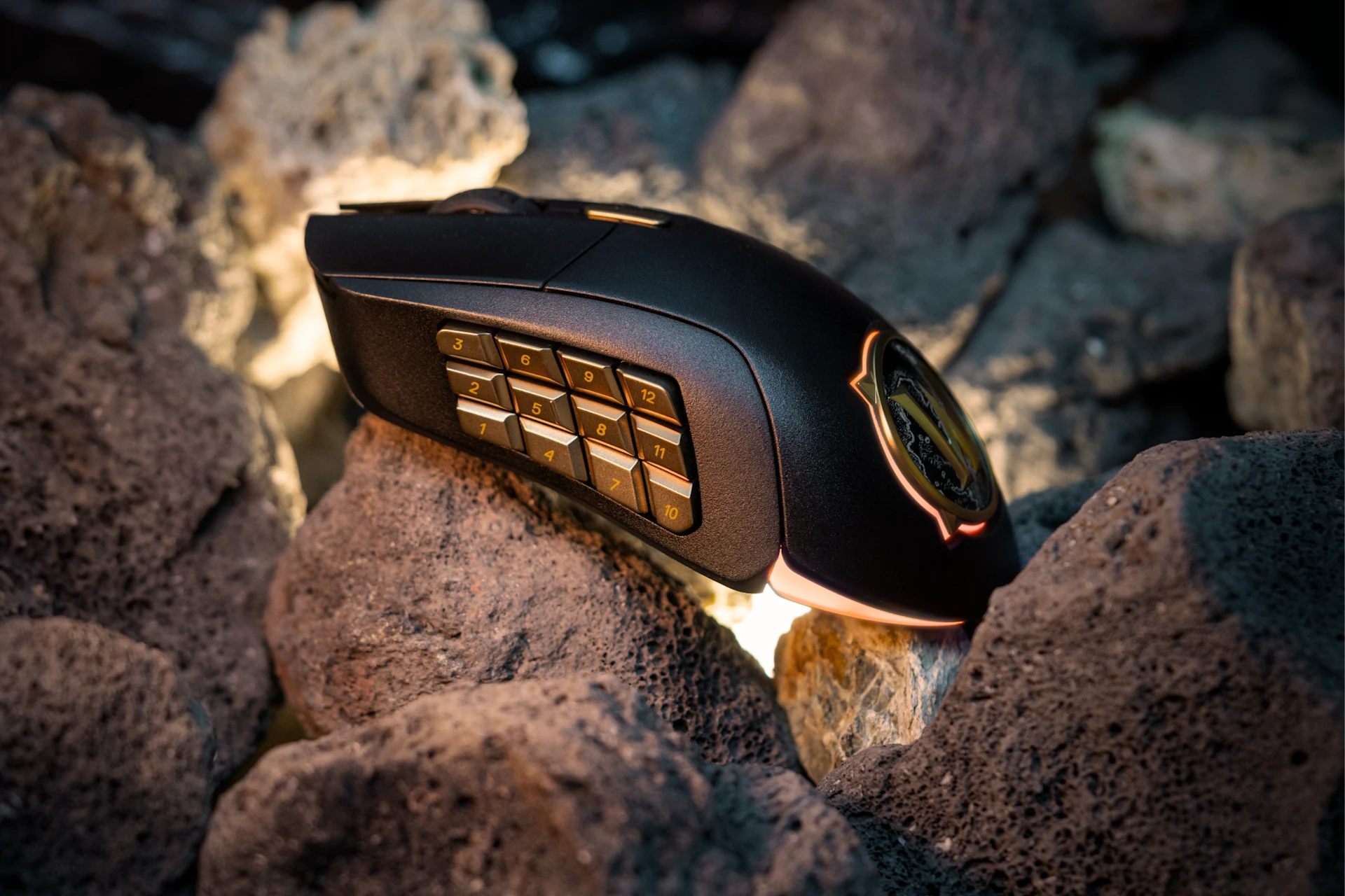 Warcraft mouse with golden buttons on the side, laying on the rocks with a little light coming out of the ground.