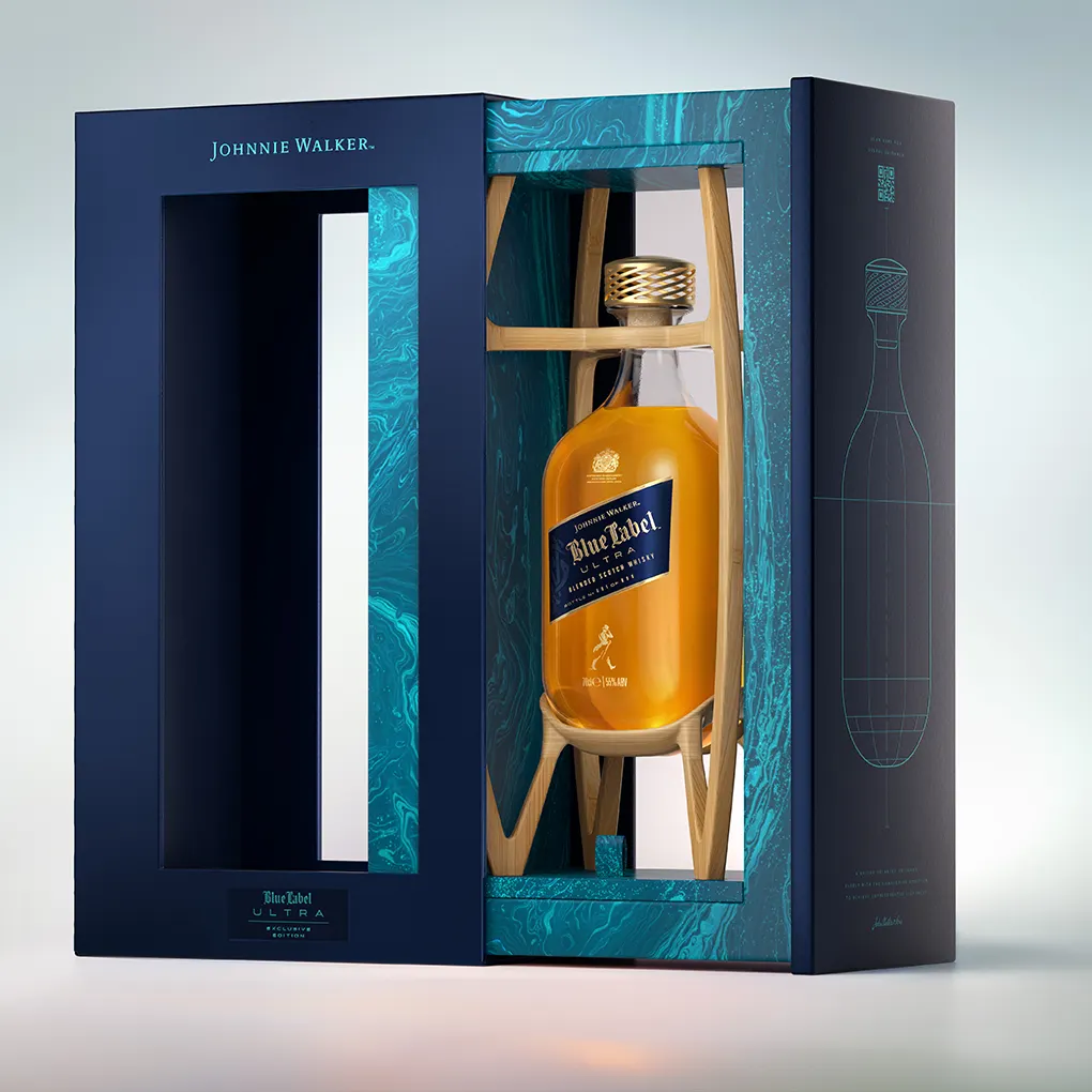 A bottle of Johnnie Walker Blue Label whisky is displayed in an elegant blue and teal gift box with a transparent window and gold design accents. The box features the Johnnie Walker branding and a line drawing of a bottle.