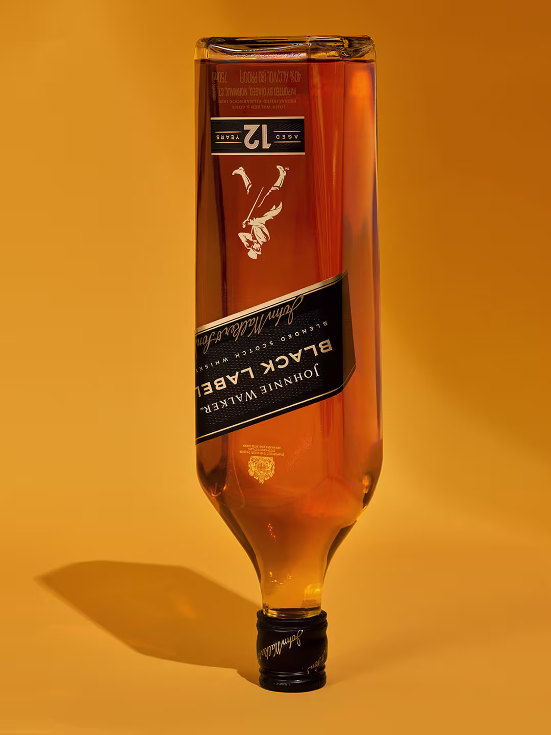 一瓶威士忌倒立在溫暖的金色背景下。標籤寫著“Black Label”和“Aged 12 Years”，頂部有一個蓋子。下面投射的陰影突出了瓶子的形狀和顏色。.