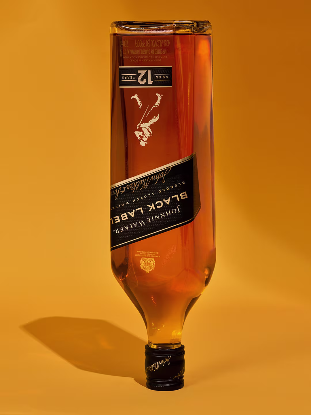 Обърната бутилка уиски Johnnie Walker Black Label на плътен оранжев фон.