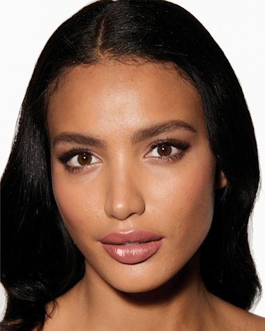Deep-tone model with brown eyes wearing a moisturising lipstick balm in a nude pink shade with a high-shine finish.