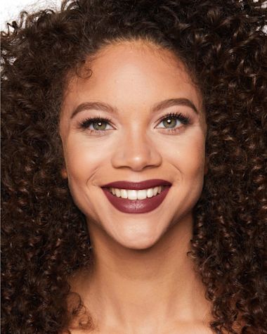 A medium-deep tone, brunette model wearing a deep berry-rose pink lipstick with a satin finish. 