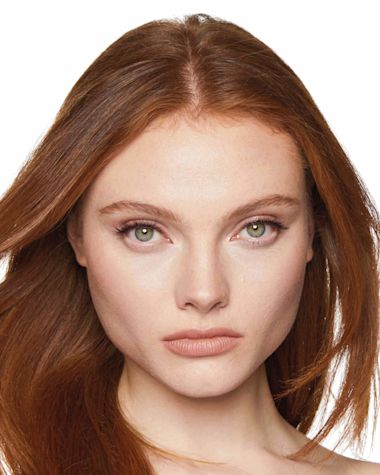 A fair-tone, auburn-hair model wearing glowy, nude makeup with bronzed skin. 