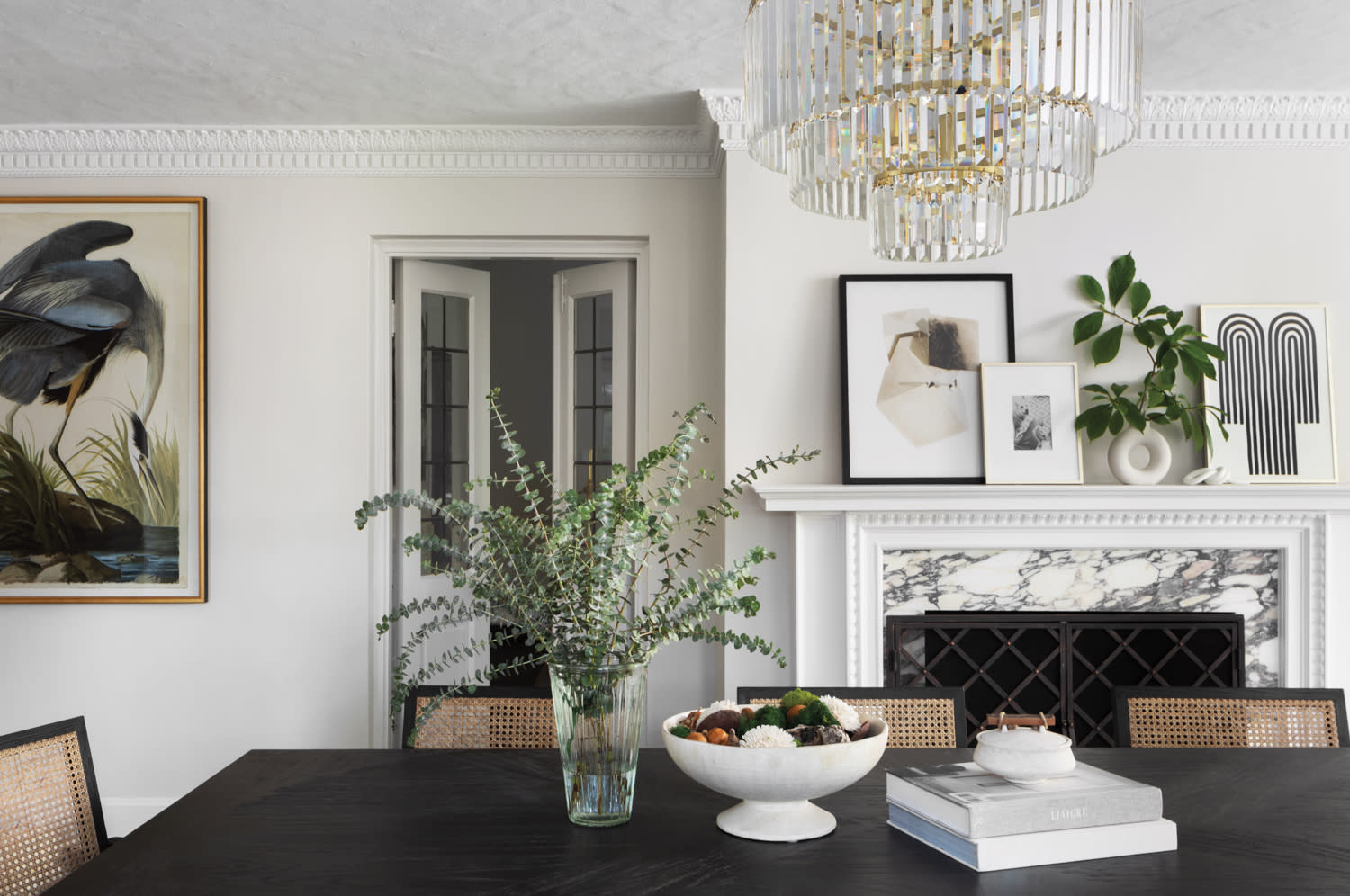 White dining room with marble fireplace, black dining table and tiered glass-and-brass chandelier